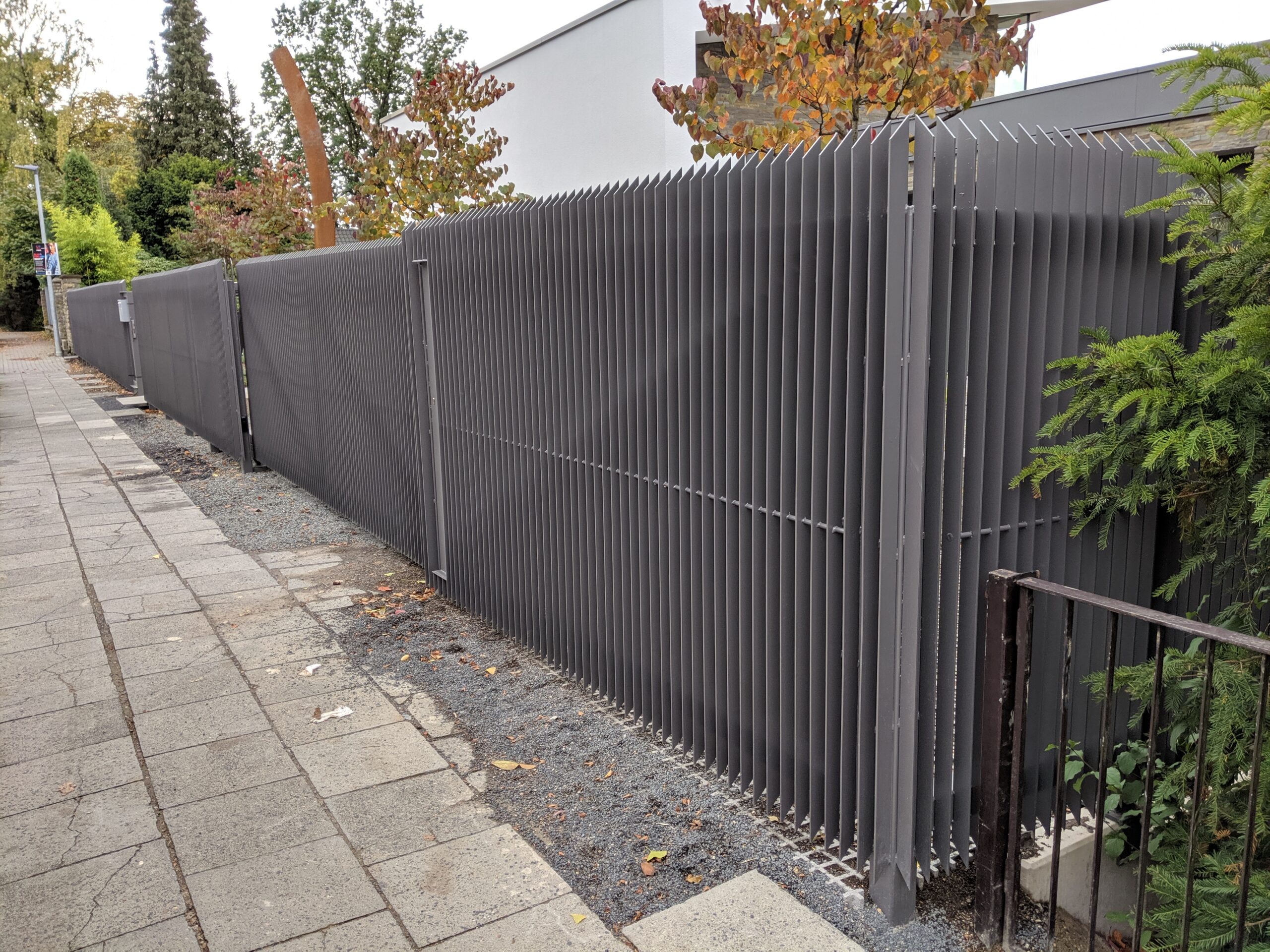 Langer Stahlzaun entlang der Grundstücksfront mit Ecke, Fahrzeugtor und separatem Fußgängertor