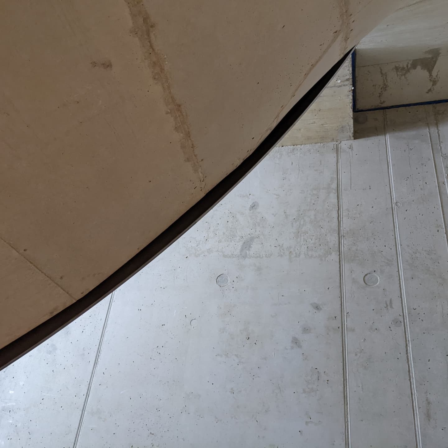Unterseite einer gewendelten Betontreppe in einem Hotel, mit Blechgeländer, das der Kurve des Betons folgt