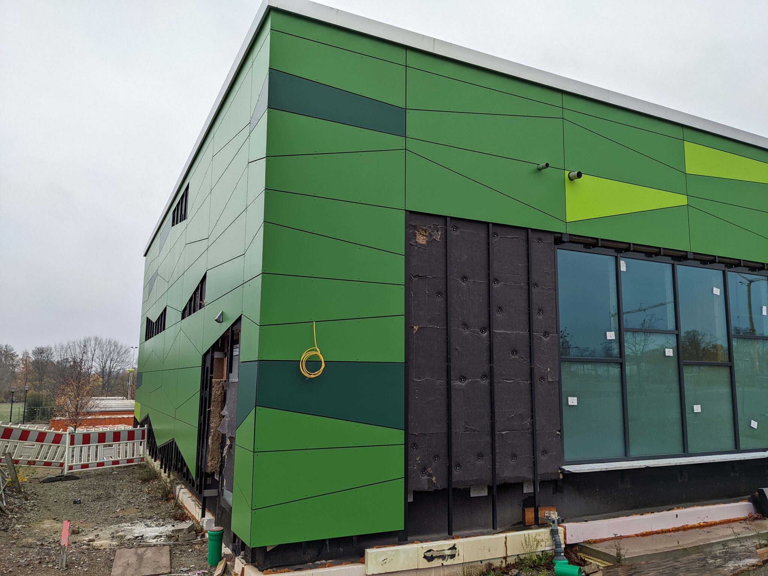 Schulfassade mit grün gestalteten Eternitpaneelen Fassadenecke einer Schule mit Eternitpaneelen in unterschiedlichen Grüntönen und unregelmäßigen Formen, noch im Bau